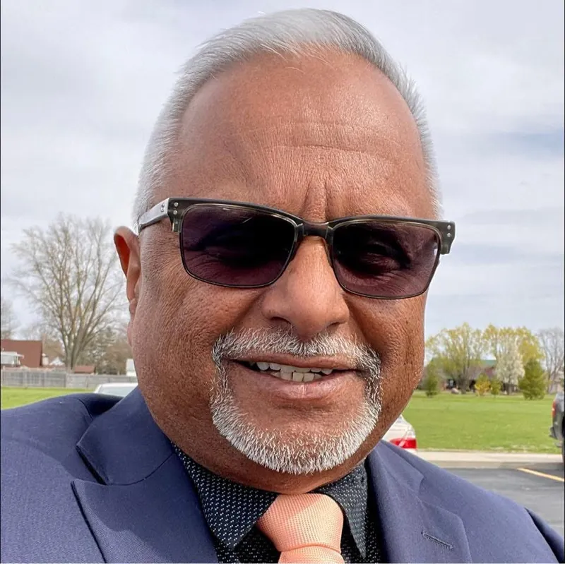 Bernie smiling outdoors in a navy suit and sunglasses