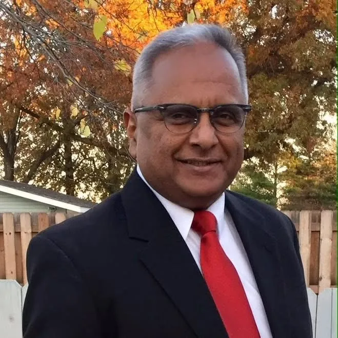 Bernie Lutchman in a dark suit and red tie in front of autumn trees